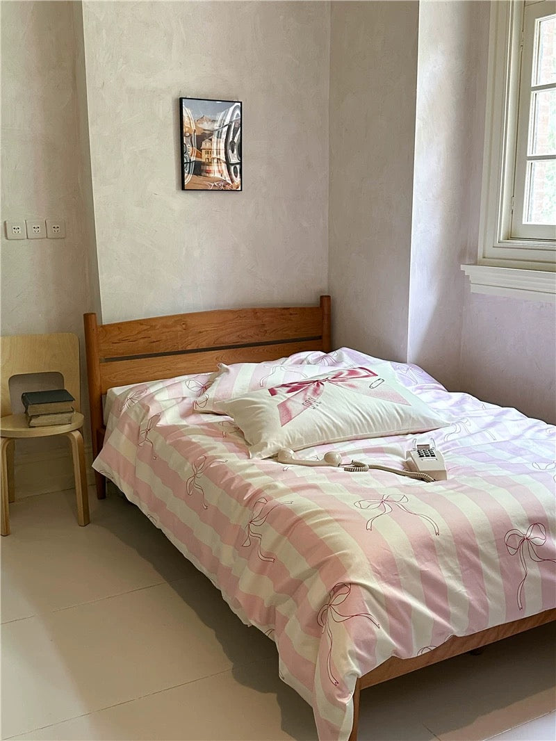 Bed with pink and white bedding in a room with a chair and wall art.