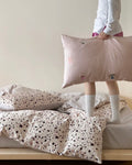 Person holding a pillow with cartoon face design on a bed with polka dot bedding.