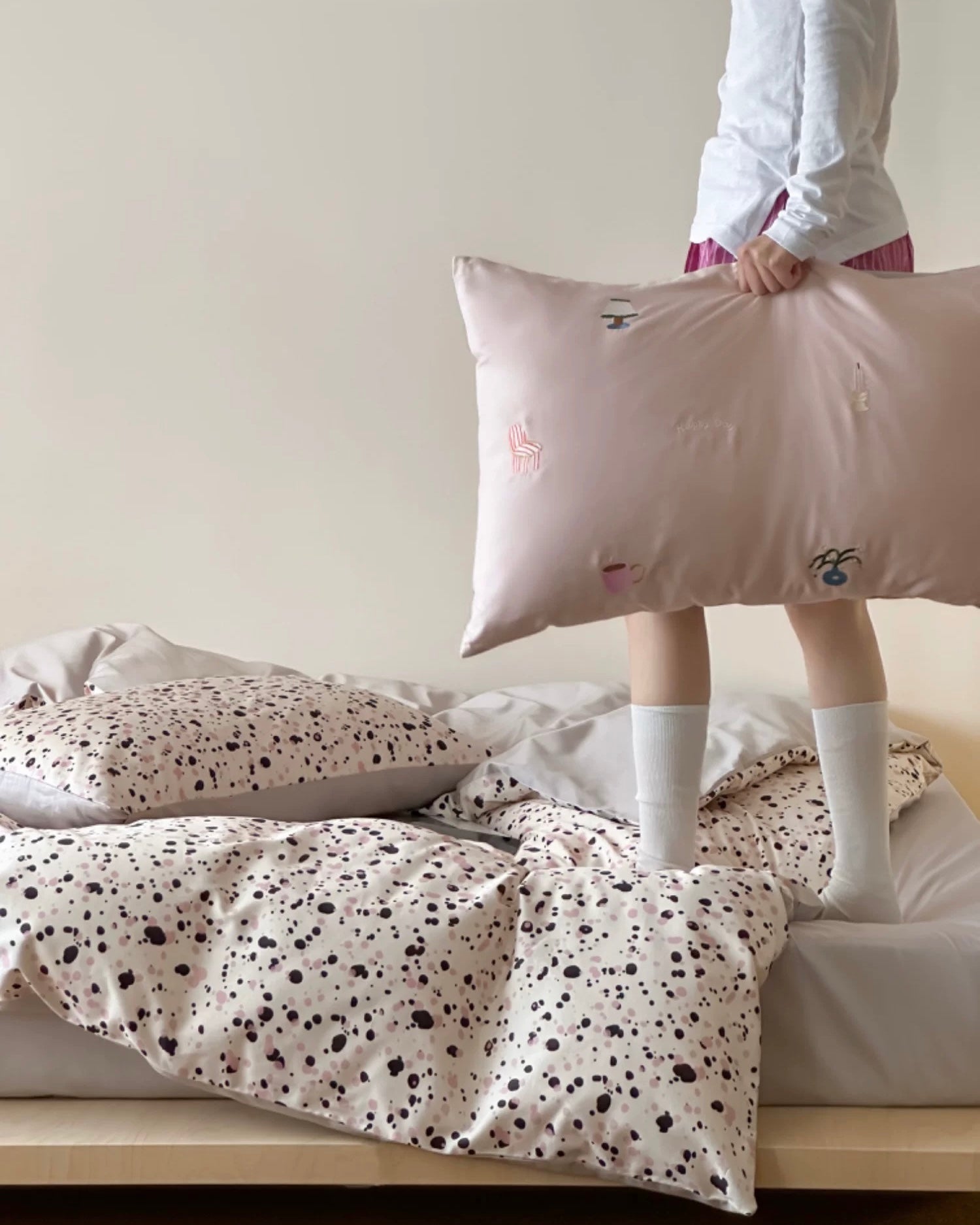 Person holding a pillow with cartoon face design on a bed with polka dot bedding.