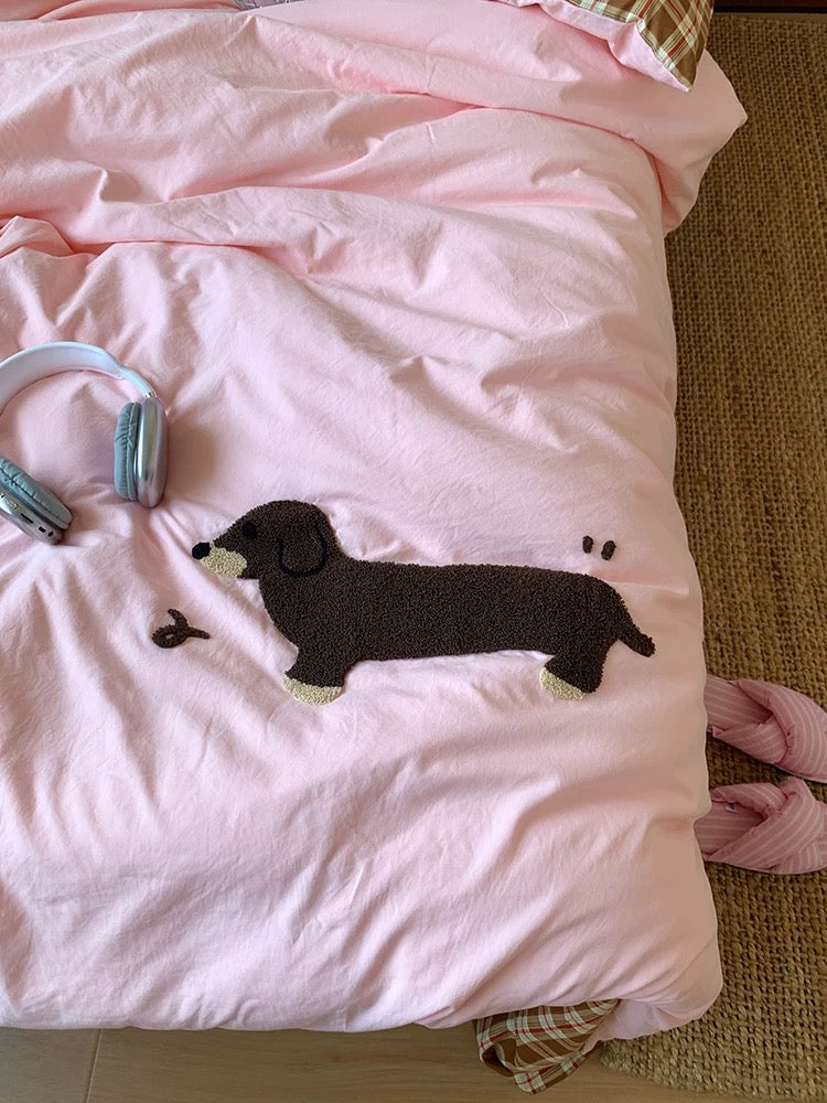 Pink blanket with a black dog applique on a bed with a brown carpet.