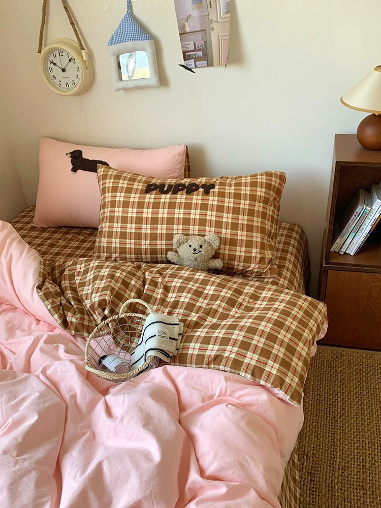 Bed with pink and plaid bedding, pillows with 'Puppy' text, and a teddy bear toy.