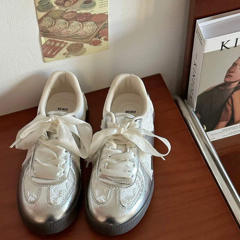 Pair of silver sneakers with white laces on a wooden surface.