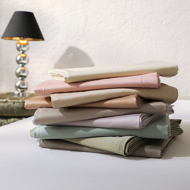 Stack of folded bed sheets in pastel colors on a white surface with a lamp in the background.