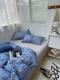 Bedroom with blue striped bedding and pillows, nightstand, and sneakers on the floor.