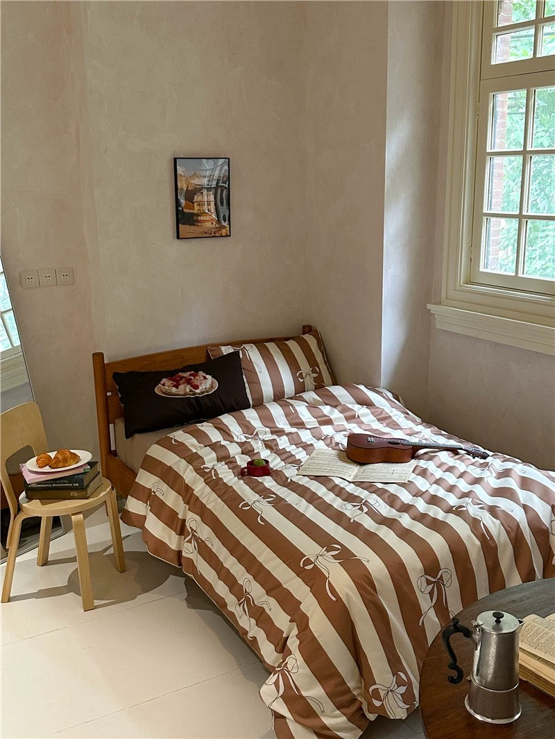 Bedroom with a bed featuring a brown and white striped comforter, a small table with items, and a window letting in natural light.
