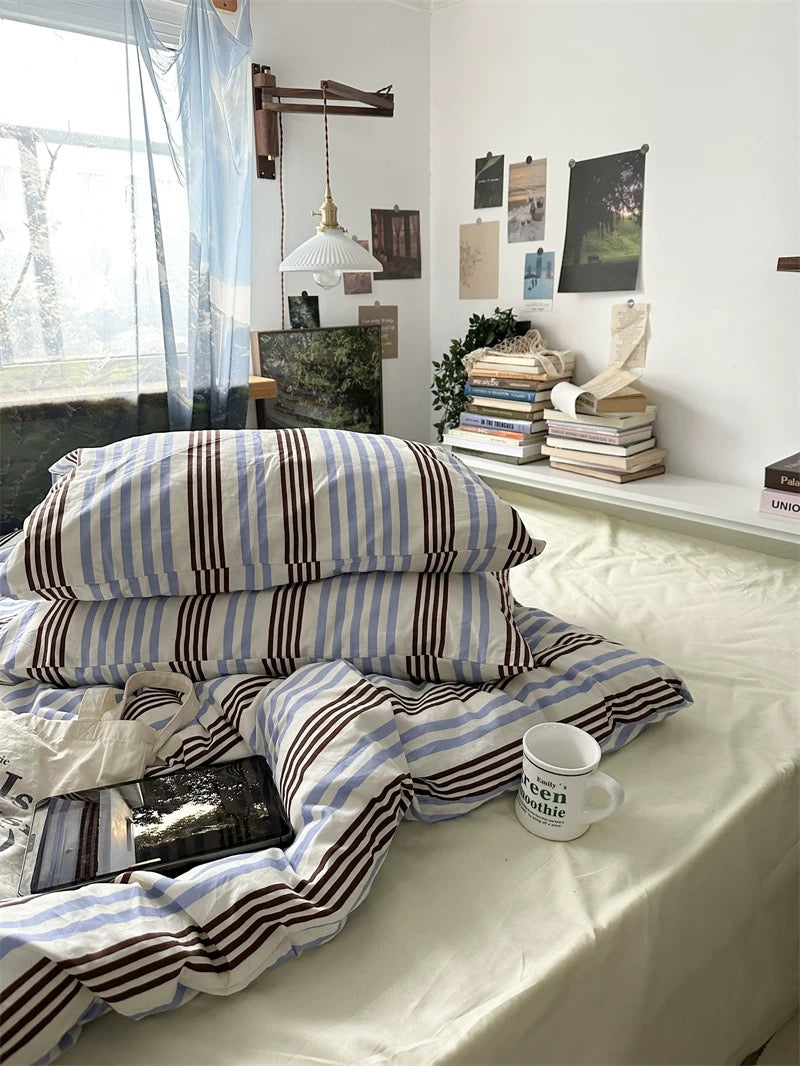 Stack of striped pillows on a bed with a cup and book in a bedroom setting.