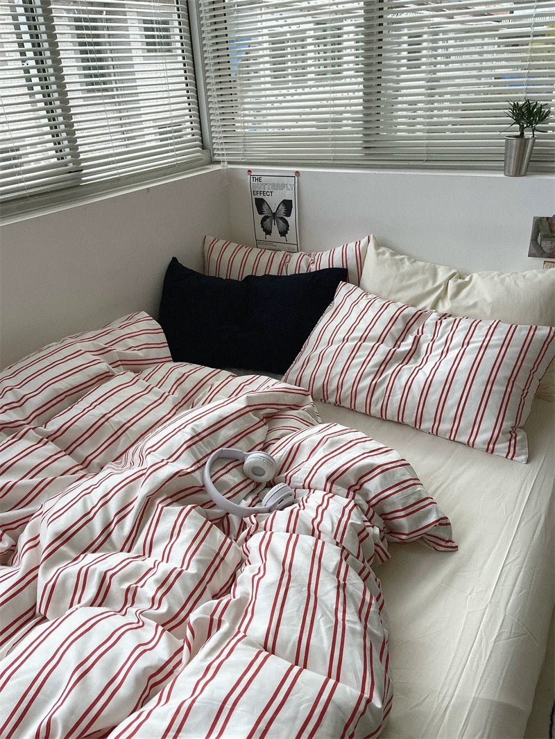 Bed with red and white striped bedding and pillows, near a window with blinds.