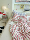 Bed with red and white striped bedding in a room with a Loewe shelf.