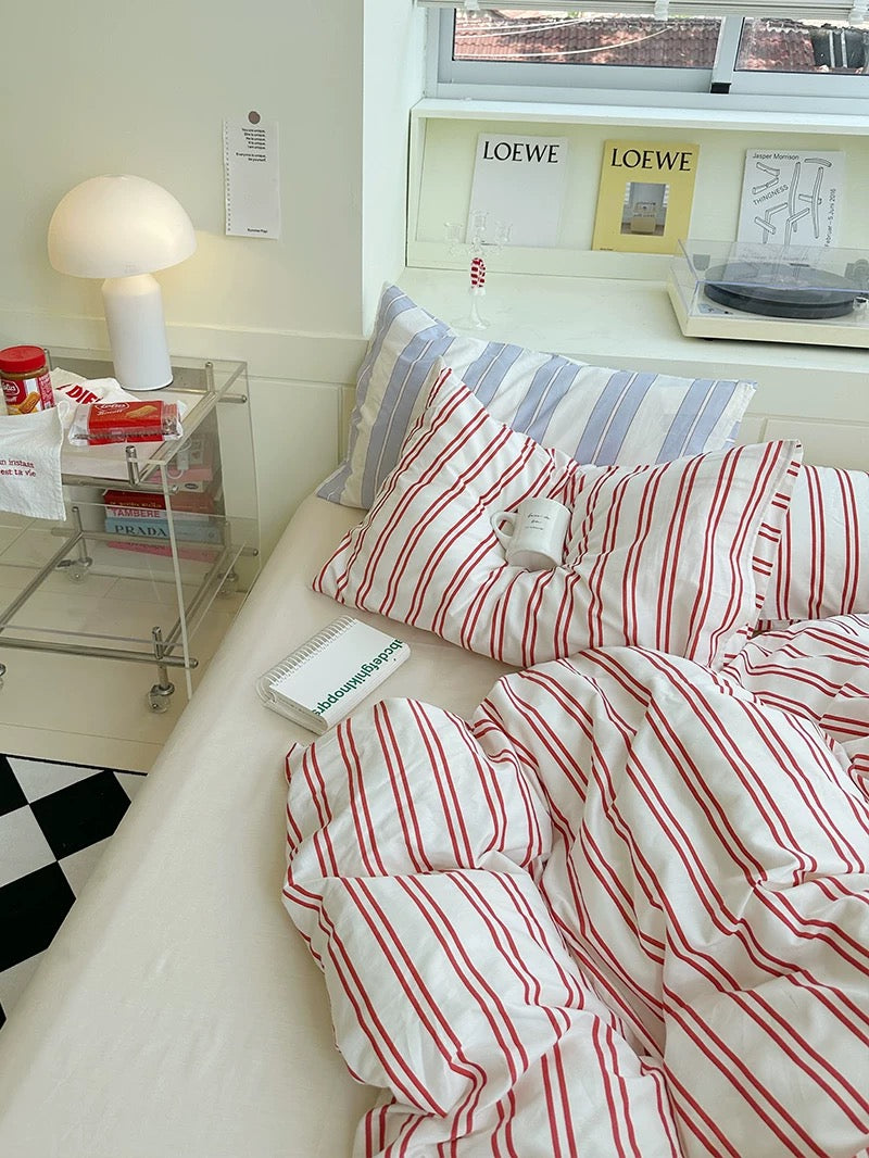 Bed with red and white striped bedding in a room with a Loewe shelf.