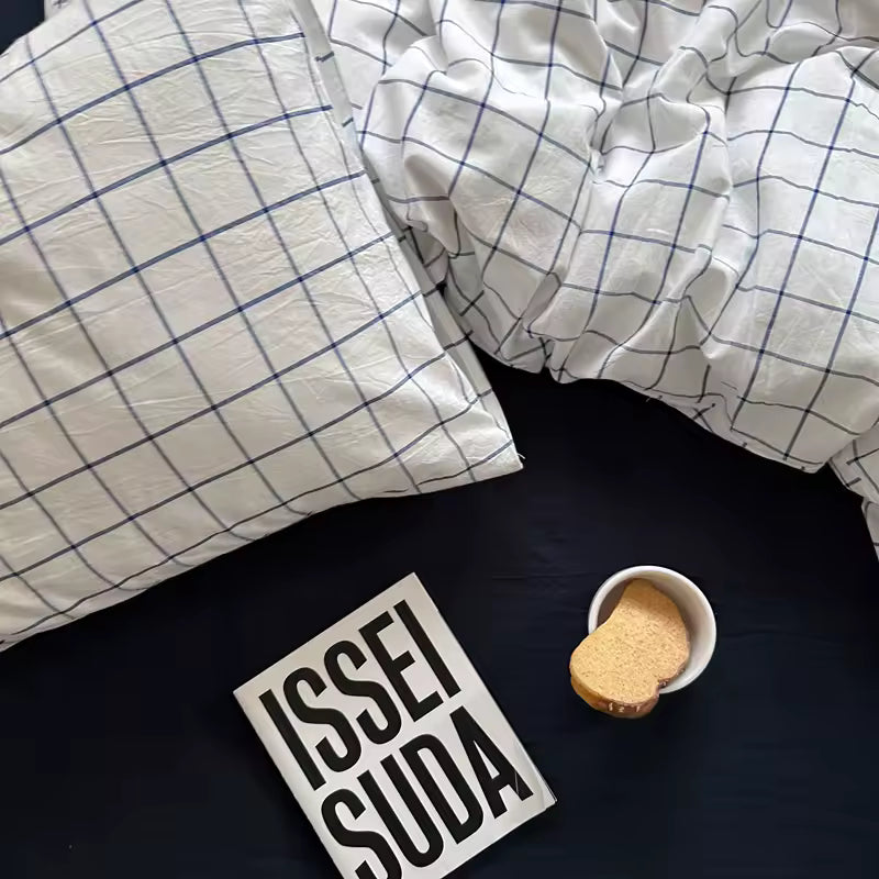 Grid-patterned pillow and duvet on a dark surface with 'ISSEI SUDA' sign and cookie.