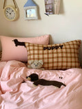 Bed with pink and plaid pillows featuring dog plush toys, a teddy bear, and a clock on the wall.