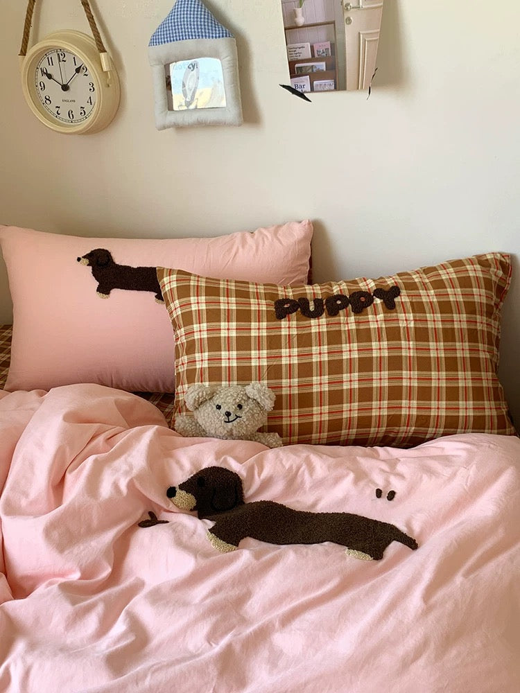 Bed with pink and plaid pillows featuring dog plush toys, a teddy bear, and a clock on the wall.