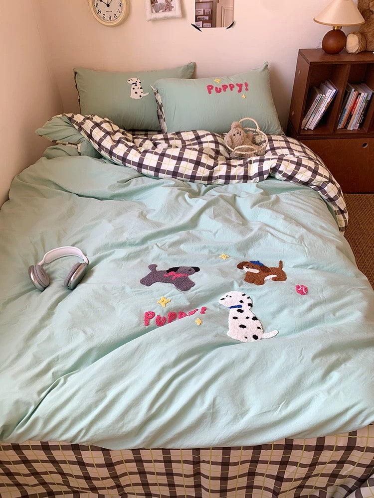 Bed with light blue comforter featuring dog illustrations, checkered blanket, and pillows with dog designs.