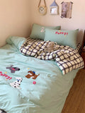 Children's bed with light blue bedding featuring dog appliqués, checkered blanket, and teddy bear.