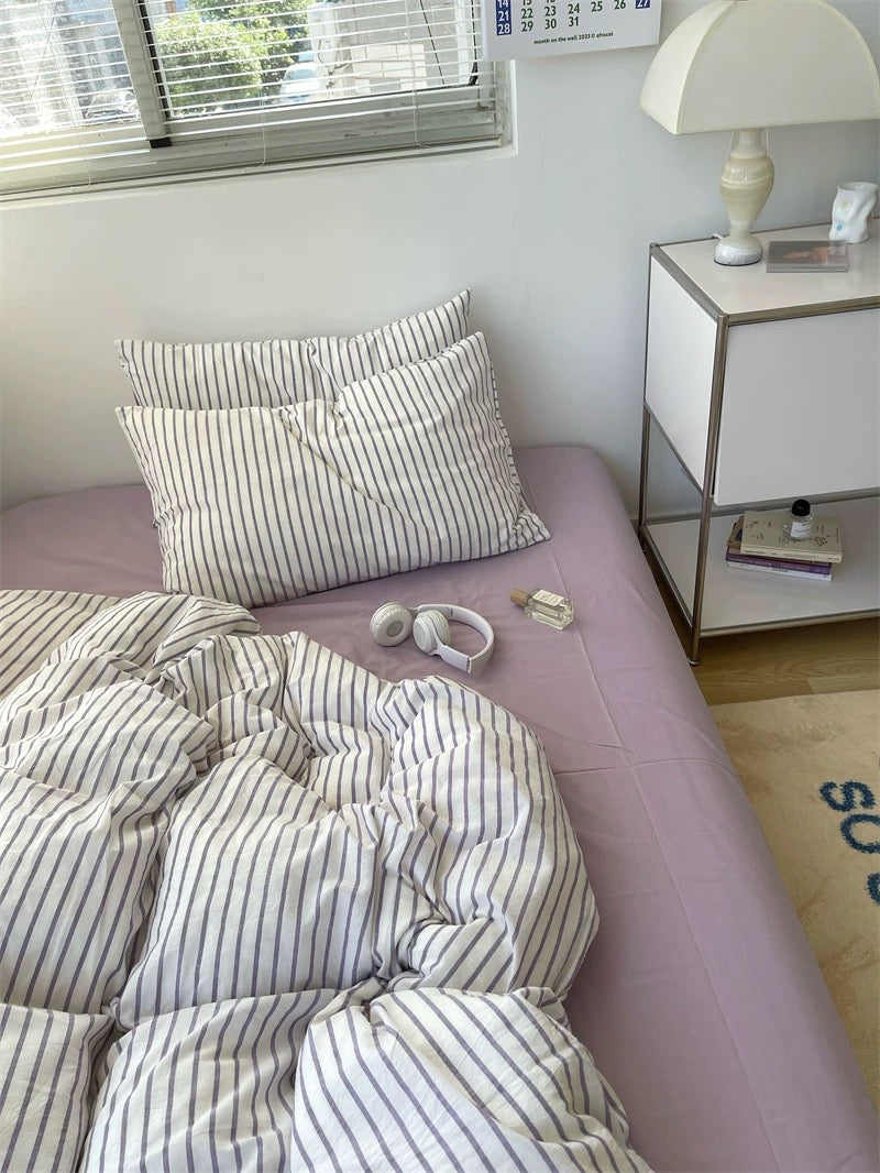 Bed with striped bedding and pillows in a room with a nightstand and lamp.