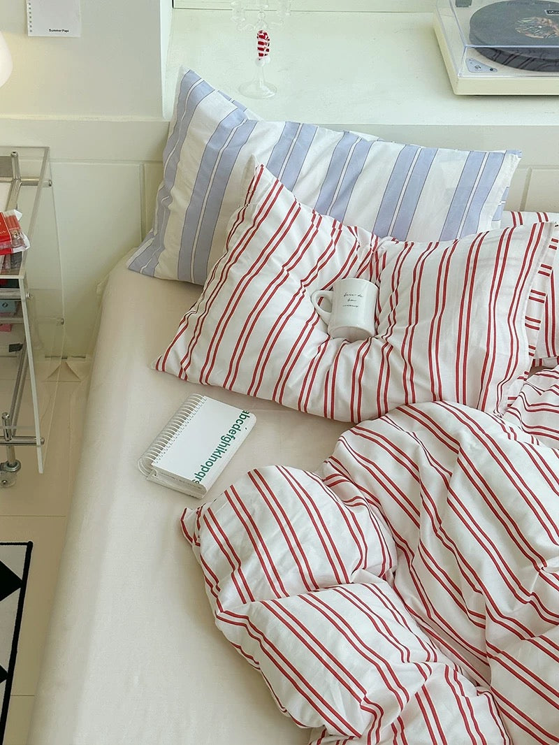 Bed with red and white striped bedding and pillows in a room with window blinds.