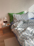 Bed with striped bedding and green pillow, nightstand with lamp and plate.