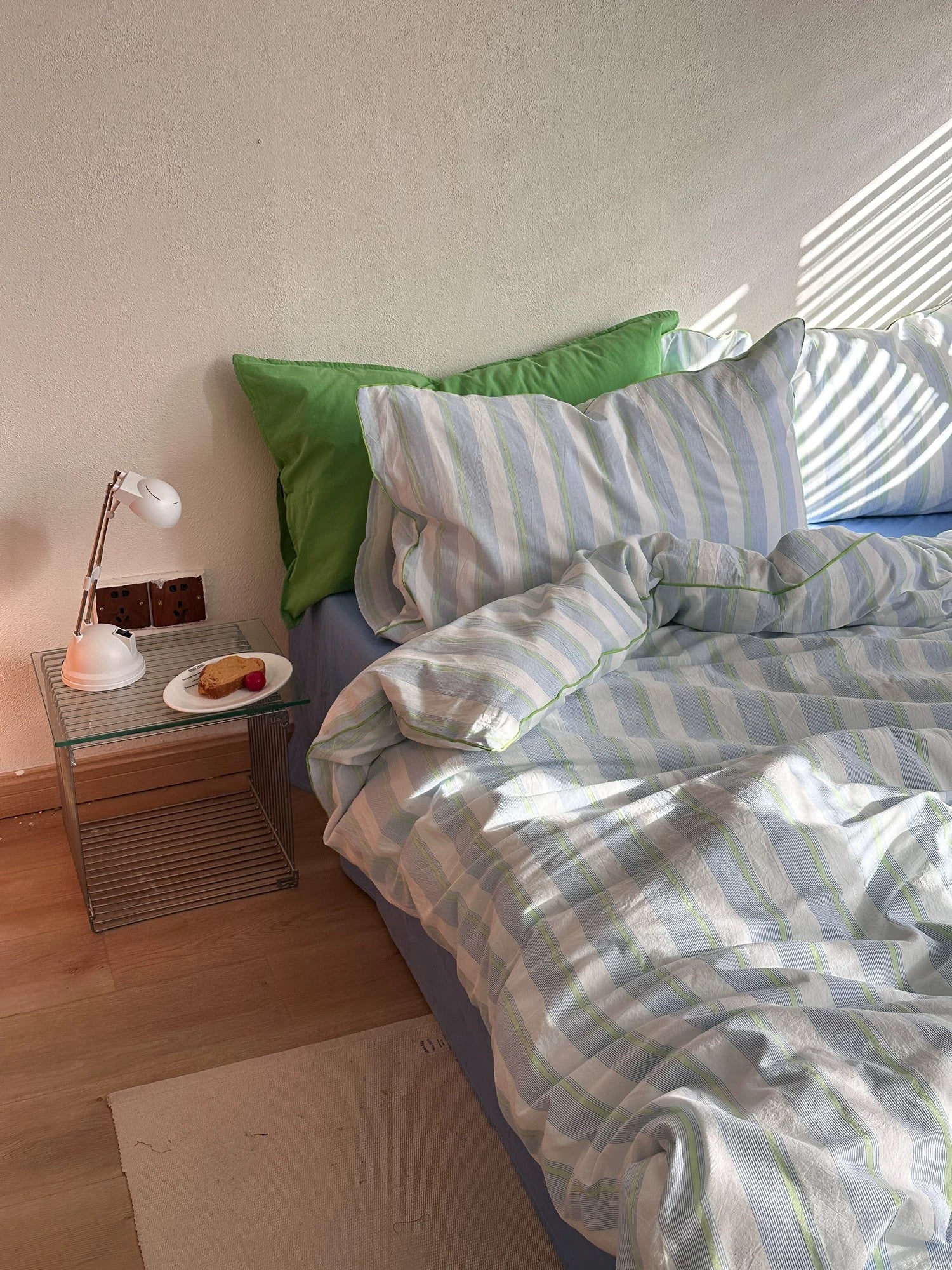 Bed with striped bedding and green pillow, nightstand with lamp and plate.