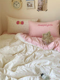 Bed with pink and white checkered bedding, teddy bear, and decorative pillows.