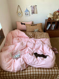 Bed with pink comforter and plaid pillows in a room with a clock and books on a shelf.
