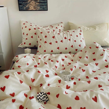 Bed with white bedding and red heart patterns, pillows, and a small black and white checkered pillow.