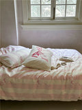 Bed with pink and white striped bedding and pillows in a room with a window.