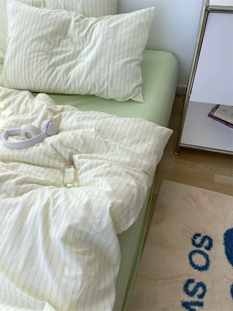Bed with white striped bedding and pillows, next to a rug with text on a wooden floor.