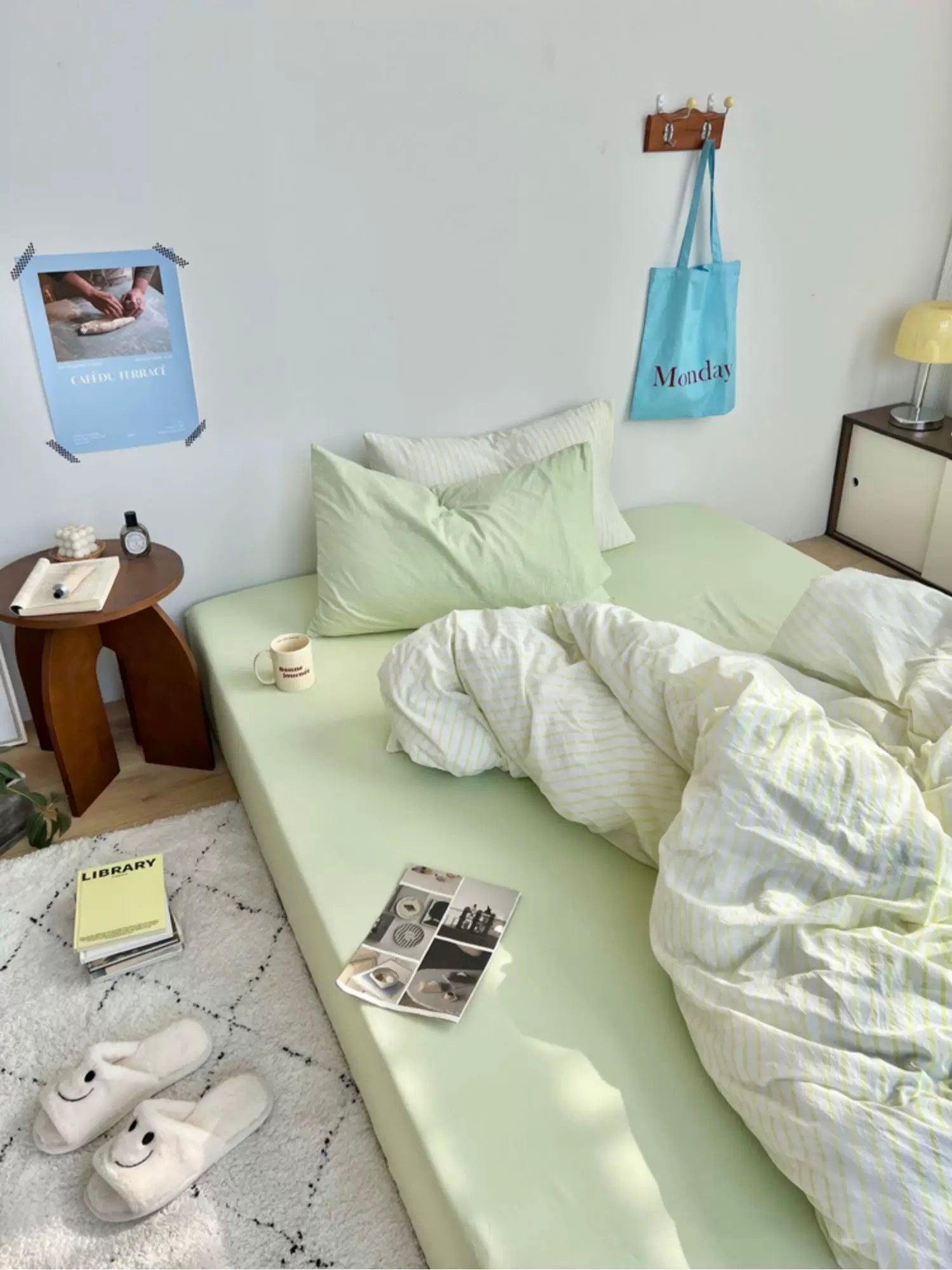 Neatly made bed with light green bedding in a room with a small table and lamp.