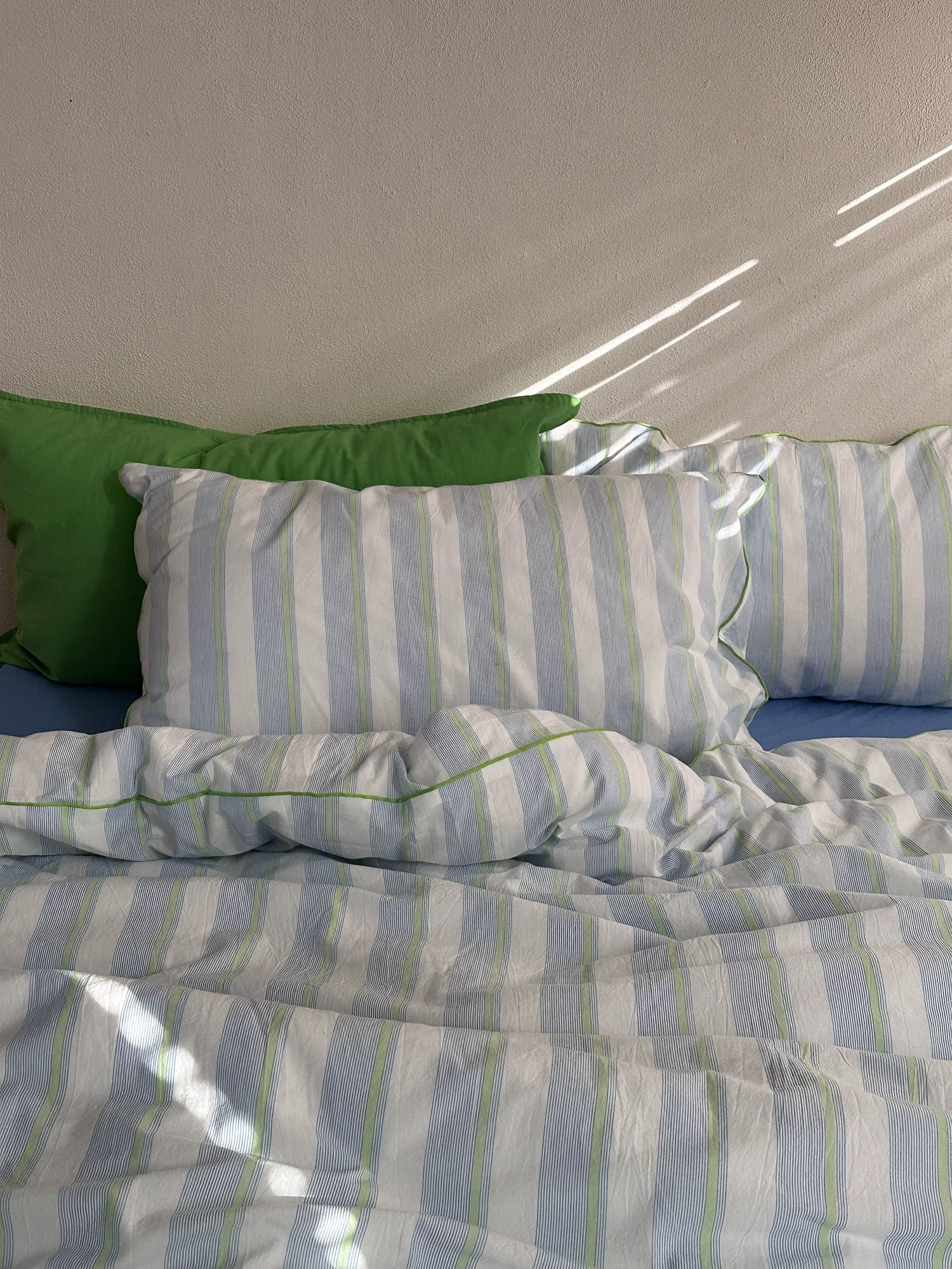 Striped bedding with a green pillow on a bed