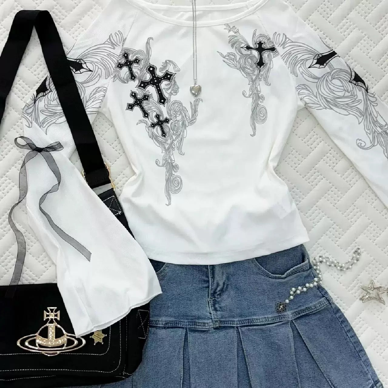 White hoodie with black embroidery, black bag with gold emblem, and blue denim skirt on a textured surface.