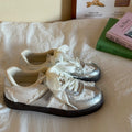 White sneakers with lace details on a white surface, with books in the background.