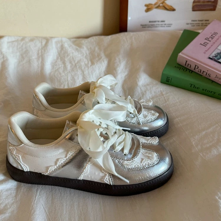 White sneakers with lace details on a white surface, with books in the background.
