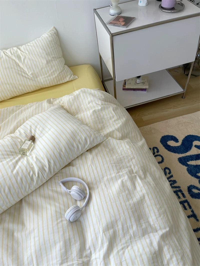 Bed with white bedding and yellow pillow, nightstand with small items in a bedroom.
