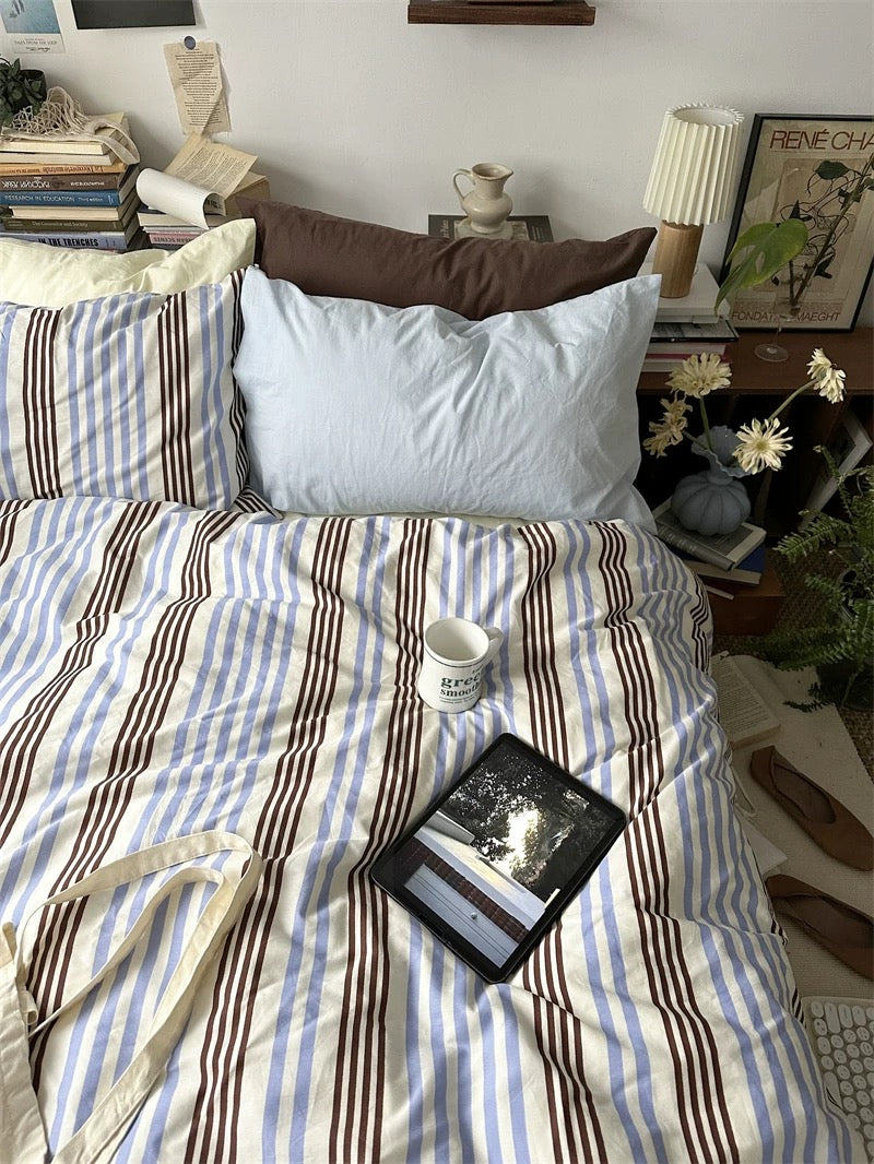 Bed with striped bedding and a tablet on a nightstand in a bedroom setting.