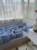 Bed with blue striped bedding in a room with large windows and a nightstand.