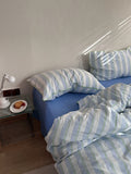 Bed with blue and white striped bedding in a room with a nightstand and lamp.