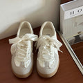 Pair of white sneakers with lace details on a wooden surface.