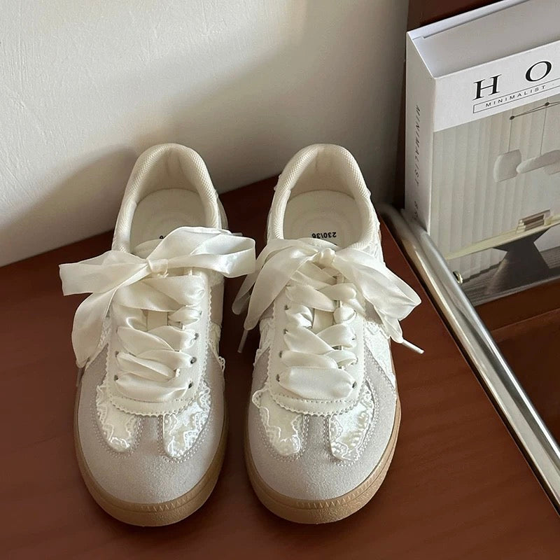 Pair of white sneakers with lace details on a wooden surface.