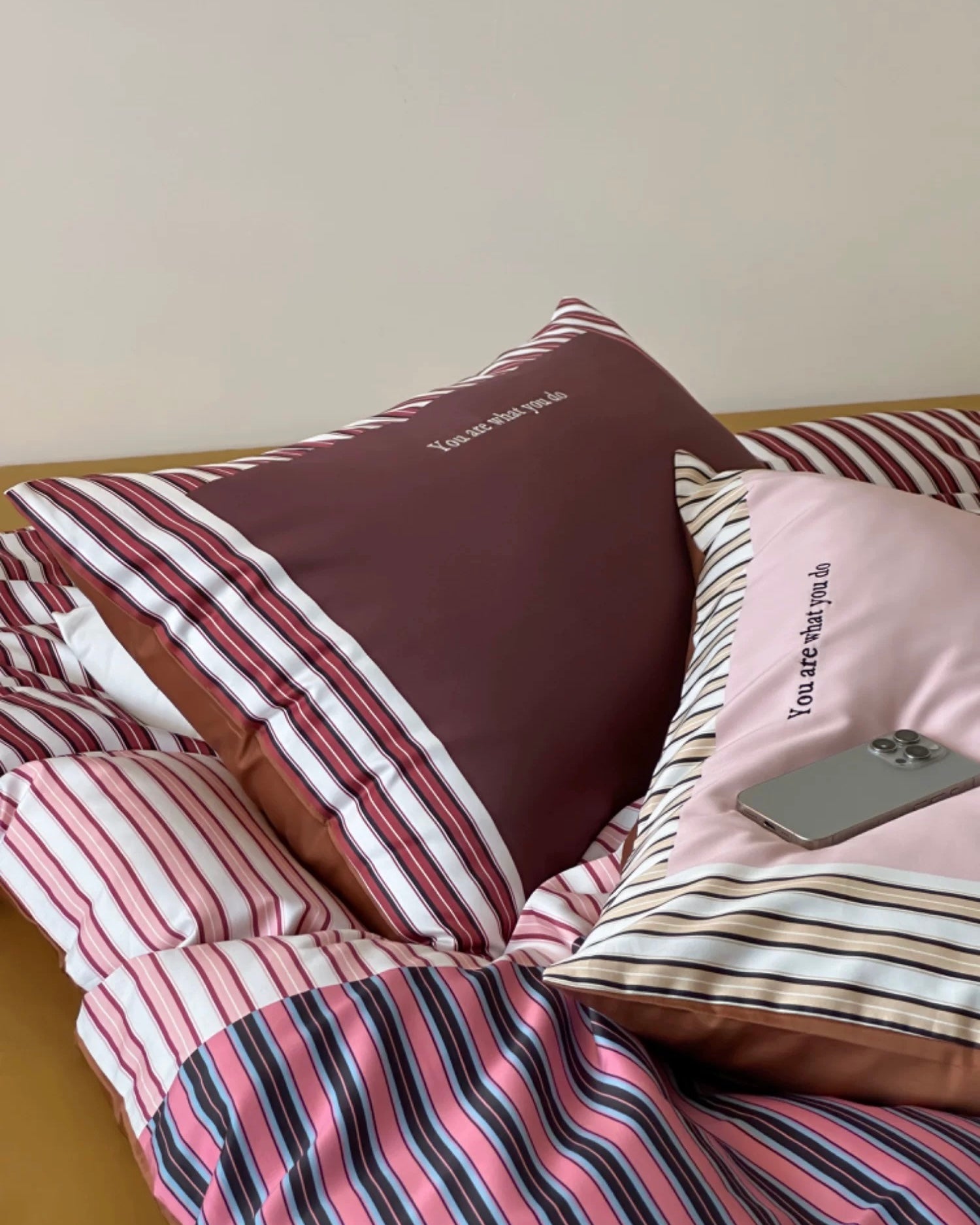Modern striped bedding with burgundy blush and brown tones styled on minimalist wooden bed frame