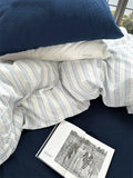 Unmade bed with striped duvet and open book on a dark surface