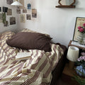 Bedroom with striped bedding and a brown pillow, nightstand with lamp and decor items.