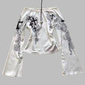 White outfit with black floral and cross designs on a textured surface