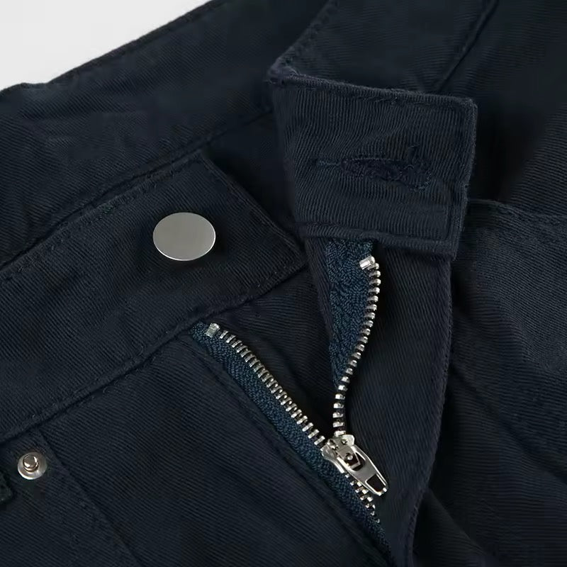 Flat lay of jeans displaying front zip, waistband, and rivet pattern.