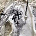 White garment with black cross designs and a heart-shaped pendant on a textured surface
