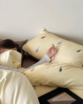 Person lying in bed with a yellow pillow featuring embroidered designs.